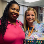 Two women posing for a photo. The woman on the right is holding a gift basket.